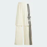 Pantalón deportivo Adidas de corte holgado en color blanco, con cintura elástica y diseño de tres tiras negras verticales en los laterales que incorporan detalles de red y el logo de la marca.
