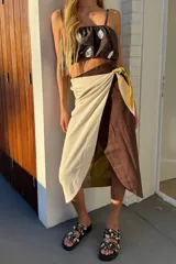 Falda envolvente tipo pareo, confeccionada en lino, con diseño cruzado y nudo lateral. La falda combina bloques de color marrón chocolate, beige crudo y un forro o capa interior en verde pistacho.