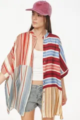 Vestido camisero corto con diseño de paneles combinados en distintos patrones de rayas verticales y horizontales, en tonos rojo, azul, beige y blanco. Posee cuello mao, cierre frontal con botones y mangas cortas caídas.
