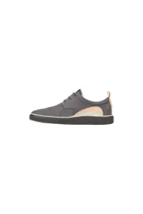 Zapato de vestir estilo derby, color gris oscuro (magnet), confeccionado en gamuza o nobuck. Presenta cordones finos y una suela de goma gruesa y texturizada de color negro con una fina línea blanca que la separa del cuerpo del zapato. Posee un tirador de cuero color camel en el talón.