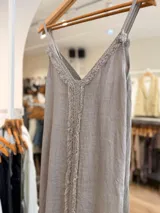 Vestido maxi de lino color blanco, con escote en V, tirantes finos regulables y detalles de flecos en el frente.