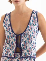 Chaleco de punto semiliviano con diseño jacquard en tonos blanco, azul y rojo, escote en V profundo y cierre frontal con tiras para anudar.