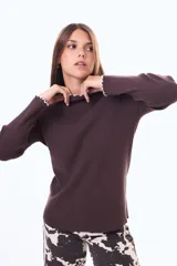 Buzo de tejido de punto color marrón chocolate, con cuello alto y puños con terminación ondulada en color blanco. De corte ajustado y manga larga.