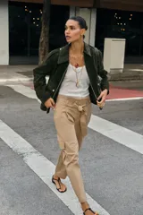 Pantalón de tiro alto estilo paperbag en color beige, con pinzas frontales y cinturón de la misma tela. Presenta bolsillos laterales tipo cargo con solapa y pernera ajustable con botones en el bajo.