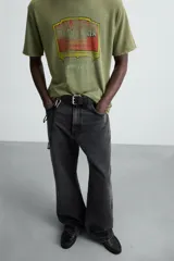 Camiseta de punto de algodón con corte relaxed fit, cuello redondo y manga corta. Color verde oliva con efecto lavado y estampado frontal con diseño gráfico en tonos rojo y amarillo.
