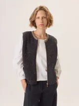 Chaleco de tejido de punto con textura en relieve, color beige, con cierre frontal y bolsillos laterales. Diseño sin mangas con cuello redondo.