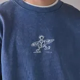 Buzo azul con efecto salt wash, cuello redondo, manga larga y puños acanalados. Presenta un estampado frontal de un surfista con la palabra "Rhythm" en blanco.