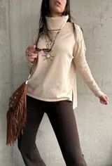 Polera de tejido de punto color beige, con cuello alto, mangas largas y aberturas laterales en el ruedo.
