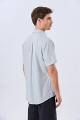 Camisa de manga corta confeccionada en mezcla de lino y algodón, con diseño de rayas verticales en tonos celeste y blanco. Cuenta con cuello camisero, botonadura frontal y bordado sutil en el pecho.