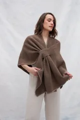 Ruana de tejido de punto industrial en color marrón, confeccionada en lana fina sin teñir. Presenta un diseño con doble ojal que permite mantener la prenda cruzada y cerrada.