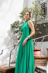 Vestido largo de gasa color verde esmeralda, con cuello halter, drapeado en el corpiño y falda plisada. Incluye lazos a los costados del cuello que permiten múltiples formas de uso.