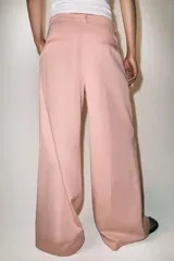 Pantalón de tiro medio con corte wide leg, confeccionado en algodón. Presenta cintura con trabillas, bolsillos laterales ocultos y detalle de pliegues en el delantero. Cierre frontal con cremallera, botón y ganchos metálicos.