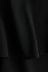 Pantalón negro de corte barrel con pollera mini acampanada superpuesta en la cintura, piernas amplias y cierre lateral.