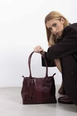 Bolso tote de cuero genuino color bordó con asas largas para hombro. Presenta una franja central con textura de cocodrilo y un adorno lateral de flecos.