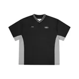 Camiseta de estilo deportivo Corteiz, color negro con paneles laterales en gris. Presenta cuello en V con detalle de rayas blancas, y logotipos estampados en el pecho.