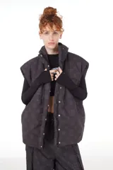 Chaleco negro con estampado de logos, cuello alto, cierre frontal con cremallera y broches a presión ocultos, bolsillos delanteros y cintura ajustable con cordón elástico. Interior de tafeta relleno de guata.