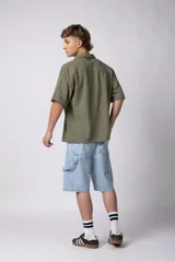 Camisa de manga corta de color verde militar, confeccionada en una mezcla de lino y viscosa. Posee un calce regular, cuello plano y cierre frontal con botones, destacándose por su textura liviana y respirable.