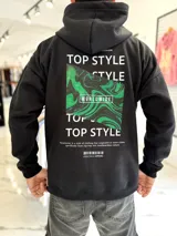 Canguro oversize negro con capucha y bolsillo tipo canguro. Presenta un estampado gráfico en la espalda con la inscripción "TOP STYLE", un rectángulo con efecto marmolado en verde y negro con la palabra "WORLDWIDE", y texto descriptivo adicional con un código de barras.