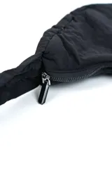 Bandolera negra acolchada de diseño curvilíneo tipo media luna, con correa ajustable integrada y cierre superior.