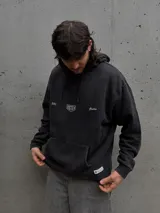 Canguro con capucha de algodón y poliéster, color negro con efecto lavado. Presenta bolsillo frontal tipo canguro, capucha con cordones ajustables y detalles gráficos estampados en el pecho.