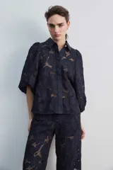 Camisa de broderie color blanco, con cuello clásico, mangas abullonadas y cierre frontal oculto.
