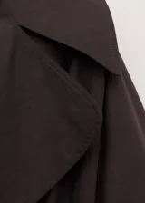 Chaqueta larga marrón de diseño recto, confeccionada en mezcla de algodón con solapas amplias, manga larga y cinturón tipo batín. Cuenta con detalle de tabla en la parte posterior y forro interior de viscosa.