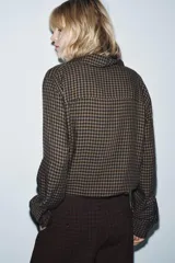 Blusa de la colección Zara Woman, confeccionada en hilatura de viscosa con estampado de cuadro vichy en tonos marrón y negro. Presenta cuello solapa, manga larga con puño y bajo ajustable con cordones. Cierre frontal con botones.