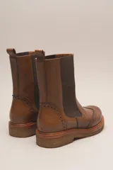 Bota tipo Chelsea de cuero vacuno color suela, con diseño brogue en la puntera y laterales. Presenta paneles elásticos laterales en color marrón oscuro, tirador trasero y suela de goma con plataforma.