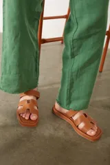 Sandalias planas de diseño minimalista en color tostado, con tiras anchas en forma de H y costuras a la vista. Poseen puntera cuadrada y suela plana.