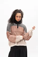 Buzo de tejido de punto con diseño a rayas horizontales en tonos tierra, negro y crema. Presenta cuello alto con cierre frontal parcial, mangas largas con puños ajustados y corte holgado.