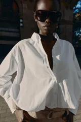 Camisa de popelín color blanco, con cuello solapa, manga larga y bajo abullonado con elástico interior. Cierre frontal con botones.