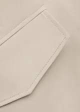 Chaqueta larga de algodón color beige, de diseño recto, manga larga, cuello camisero y cierre delantero con botones ocultos. Cuenta con dos bolsillos laterales con solapa.