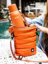 Bolso matero color naranja con diseño capitoneado, correa larga regulable y logo de la marca en la parte inferior.