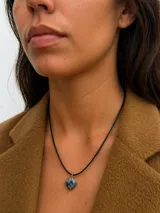 Collar de cordón negro con dije de corazón de piedra natural engarzado en borde dorado.