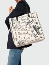 Bolso tipo tote de lona color crudo con estampado de grafitis en negro y asas de cuero negro.