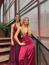 Vestido largo sin mangas con escote en V halter y aberturas laterales (cut-outs) en la cintura. El cuerpo superior presenta un llamativo diseño estampado multicolor, mientras que la falda larga es de tejido texturizado brillante en color verde esmeralda con inserciones godet en el ruedo.