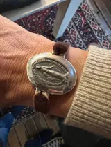 Pulsera con dije central ovalado de metal plateado que presenta la imagen de la Virgen Milagrosa en relieve con inscripciones en francés. La pulsera cuenta con una banda de terciopelo elástico para un ajuste cómodo.