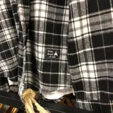 Sobrecamisa de franela a cuadros blancos, negros y grises, de manga larga, con cuello camisero, cierre abotonado y bolsillo en el pecho.