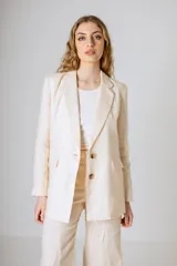 Blazer color beige confeccionado en lino, con solapas clásicas, cierre frontal de dos botones y bolsillos con solapa en los laterales.