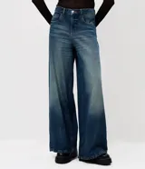Pantalón de jean con corte super wide leg y tiro medio. Presenta un lavado uniforme con efecto levemente marcado, cintura con pasantes, cierre frontal con botón y cremallera, y bolsillos funcionales. Incluye remaches metálicos decorativos en forma de corazón.