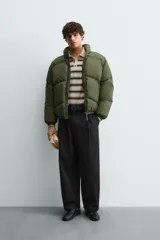 Cazadora acolchada tipo puffer de corte relajado, color verde militar. Presenta cuello subido, cierre frontal con cremallera, bolsillos laterales con cierre y puños elásticos.