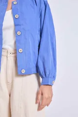 Cazadora azul de manga larga con puños elásticos, cuello redondo sin solapas y cierre frontal con botones grandes de color claro.
