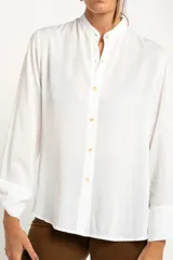 Camisa blanca de manga larga con cuello mao y cierre frontal con botones. Las mangas tienen nudos decorativos en los puños.