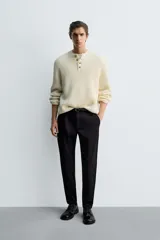 Pantalón de corte slim fit y color negro, confeccionado en tejido elástico. Cuenta con cintura elástica, trabillas, bolsillos frontales y cierre con cremallera y botón.