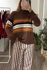Sweater de tejido de punto con cuello alto y mangas largas. Presenta un diseño de rayas horizontales en tonos marrón, negro, blanco y mostaza en la parte frontal y en las mangas.