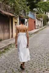 Vestido midi de color blanco con escote en pico y tirantes finos. Presenta un diseño con frunces en la cintura y detalle de lazada frontal.