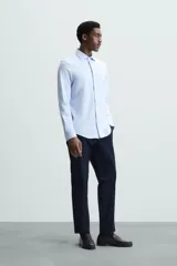 Camisa de manga larga, color celeste con finas rayas verticales blancas, cuello italiano y cierre frontal de botones.