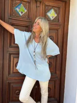 Blusa de textura arrugada en color celeste, con cuello redondo, mangas cortas amplias y corte holgado.