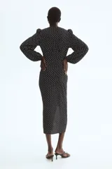 Vestido midi negro con estampado de lunares blancos, escote en V pronunciado, botones forrados frontales y mangas largas abullonadas con puños elásticos.