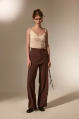 Pantalon de corte recto y tiro alto, confeccionado en tela texturizada color marrón, con detalle de falda superpuesta en la cintura.